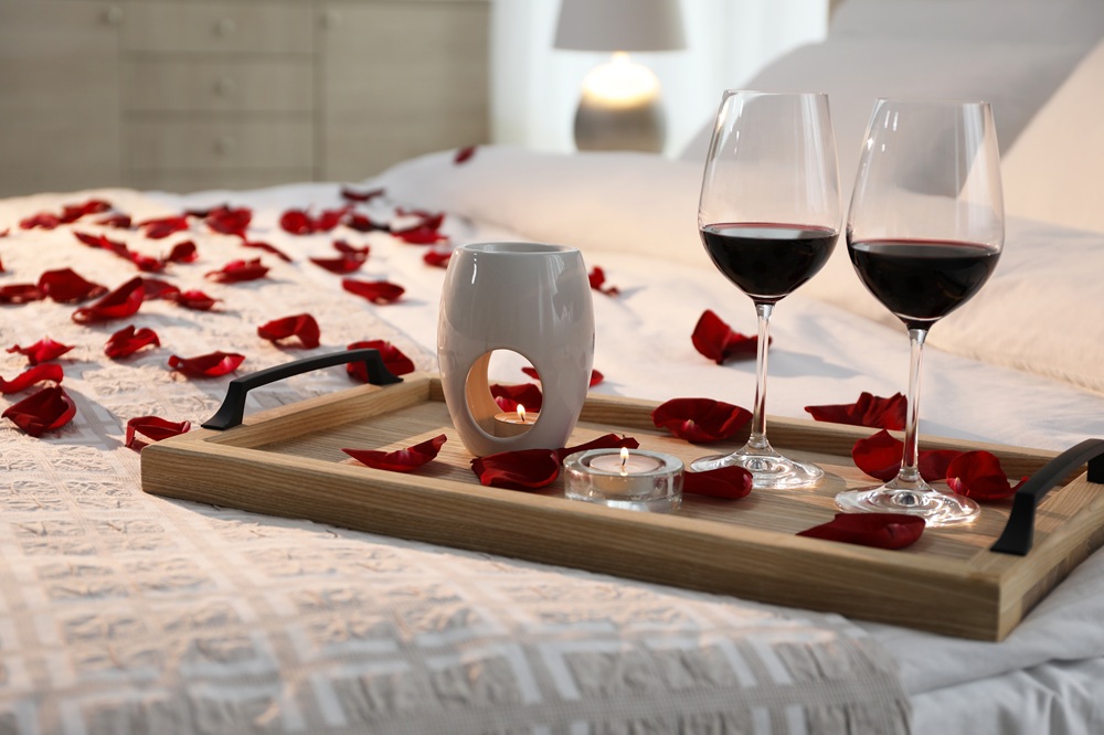 letto decorato per San Valentino con bicchieri di vino e candele su un vassoio