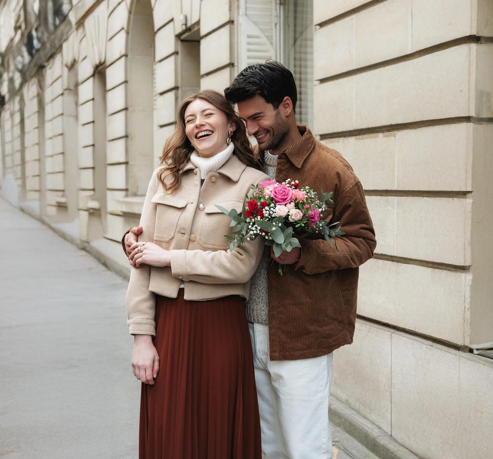 Coppia che ride per strada con un mazzo di fiori nelle mani dell'uomo