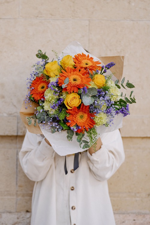 persona che tiene in mano un mazzo di fiori colorati arancioni, gialli, verdi