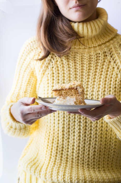 Donna con maglione giallo che tiene in mano un piattino con una fetta di torta mimosa