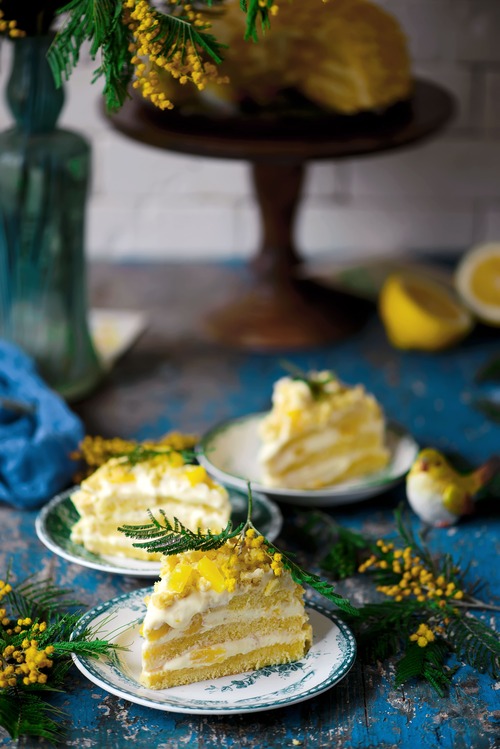 Due fette di torta mimosa con crema e pan di Spagna, servite su piatti decorati con limone e mimosa