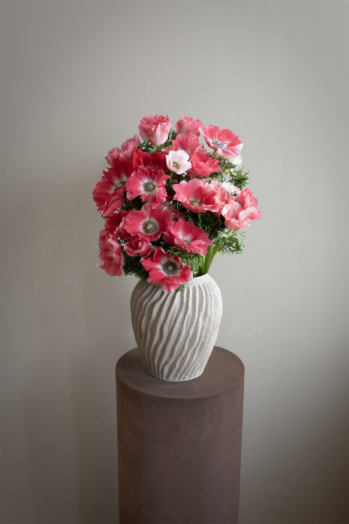 Composizione di anemoni rosa in vaso decorativo appoggiata su un piedistallo in un ambiente minimal