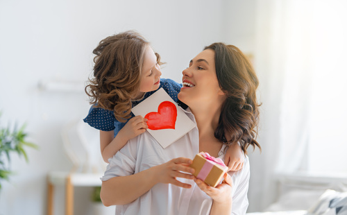 Una bambina che regala alla mamma un biglietto scritto a mano per la sua festa