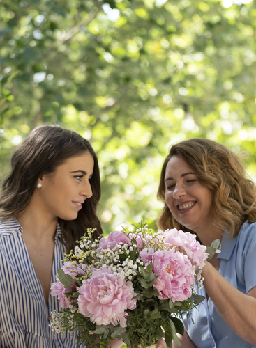 Mamma e figlia sorridenti tengono in mano un bouquet di fiori rosa in un giardino