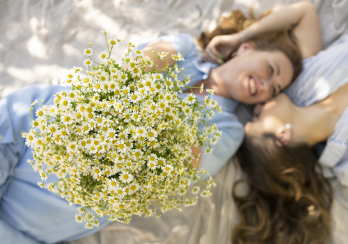 Donna sdraiata accanto a un'altra mentre tiene in mano un grande bouquet di margherite bianche.